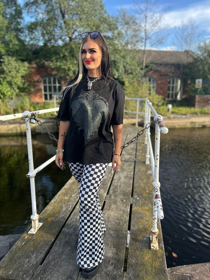 Model leaning on railing, wearing ANG3L “Poison & Beauty” Oversized Gothic Tee, styled with alternative streetwear accessories.
