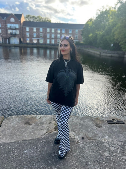 Model standing in ANG3L “Poison & Beauty” Oversized Gothic Tee, oversized fit shown, paired with checkered trousers.
